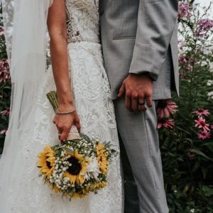 A bride and groom holding hands in front of flowers.