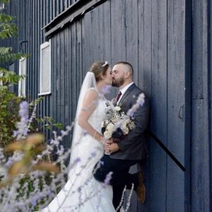 A bride and groom kissing in front of a barn.