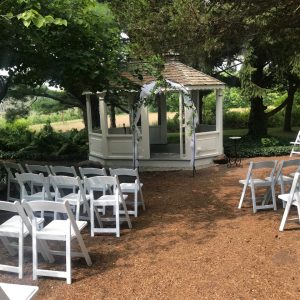 A white gazebo with chairs set up for an outdoor wedding.